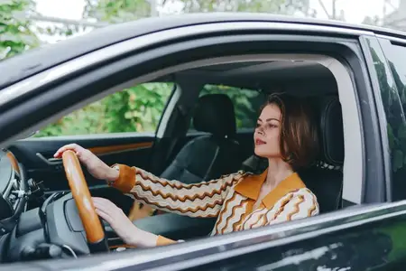 Непринужденная автомобильная сцена со стильной водительницей в уютном свитере, городским фоном, дневным освещением, настроением независимости и контроля