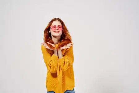 Женщина в жёлтом свитере с укладкой, модные очки, позирует в студии