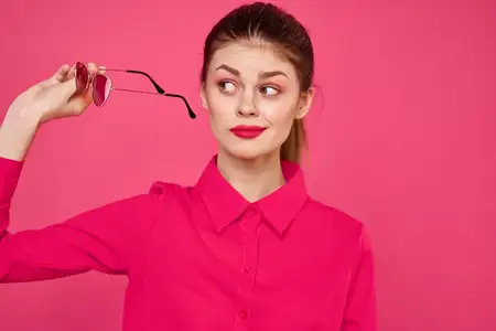 Модная женщина в розовой рубашке с очками в руках на изолированном фоне, обрезанный вид