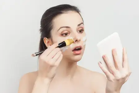 Симпатичная женщина наносит кисточкой крем на лицо, уход за кожей, омоложение