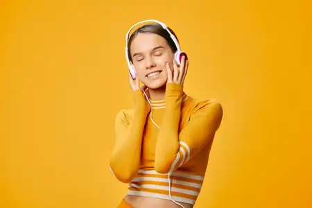 Спортивная женщина в оранжевом костюме наслаждается тренировочной атмосферой, в наушниках, с закрытыми глазами, бодрое настроение, минималистичная студийная обстановка и яркий цвет