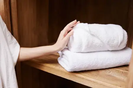 Мягкая женщина держит стопку белых полотенец на фоне отеля