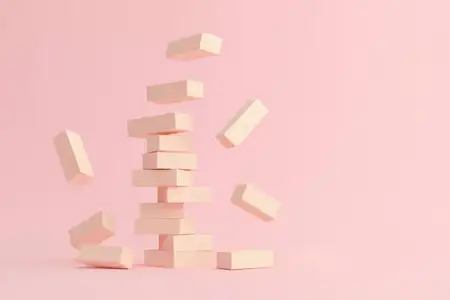 Яркая композиция из деревянных блоков, балансирующих на мягком розовом фоне, символизирующая креативность и нестабильность в дизайне