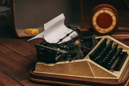 Винтажная печатная машинка, белый лист бумаги, деревянный фон, ретро-изобретение
