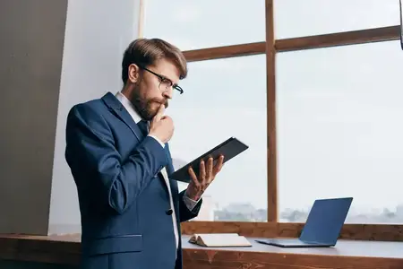 Предприниматель стоит у окна с планшетом в офисе