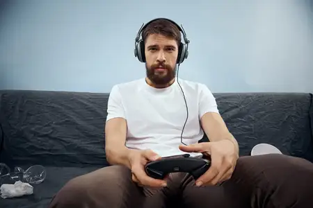 Мужчина сидит на диване в наушниках с геймпадом, играет, еда, досуг, технологии, образ жизни