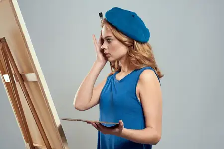 Женщина-художница в синем берете с палитрой рисует на мольберте