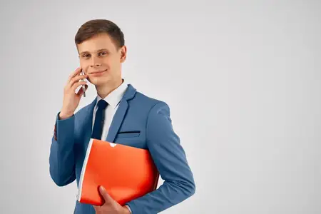 Мужчина в костюме держит в руках красную папку и телефон, используя коммуникационные технологии
