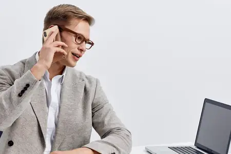 Бизнесмен пользуется мобильным телефоном на работе в современном офисном помещении с ноутбуком, одет в пиджак