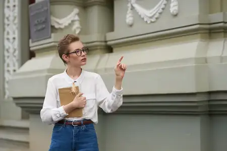 Студент в очках прогуливается по городу с книгой в руках, посвящая время образованию