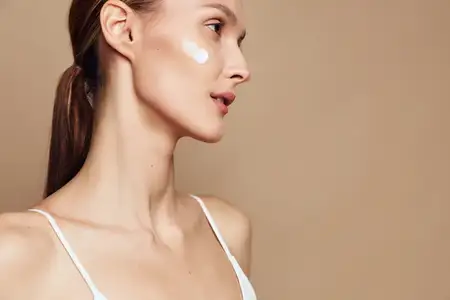 Крупный план женщины с пятнышком крема на щеке, демонстрирующий уход за кожей лица