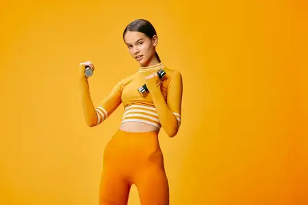 Спортивная девушка выполняет легкую силовую тренировку в укороченном топе с длинным рукавом и леггинсах с высокой талией, аккуратный хвост, сосредоточенное выражение лица и сбалансированная стойка…