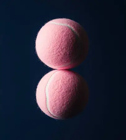 Это изображение показывает два розовых теннисных мяча на гладкой отражающей поверхности, подчеркивая их текстуру и яркий цвет на темно-синем фоне, что идеально подходит для спортивного дизайна