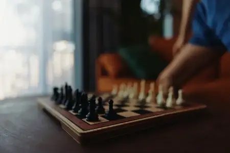 Стратегическая игра в шахматы, в которую играет человек за столом перед окном