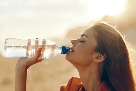 Женщина пьёт воду на открытом воздухе в летний солнечный день