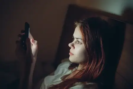 Женщина лежит в постели с телефоном в руках