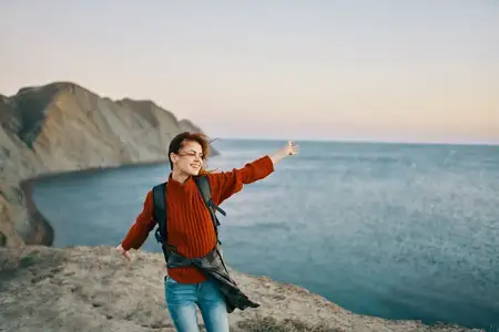 Женщина-туристка жестикулирует руками в горах у моря на природе, вид сверху