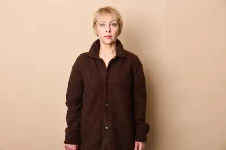 Пожилая женщина в пальто стоит в студии на бежевом фоне