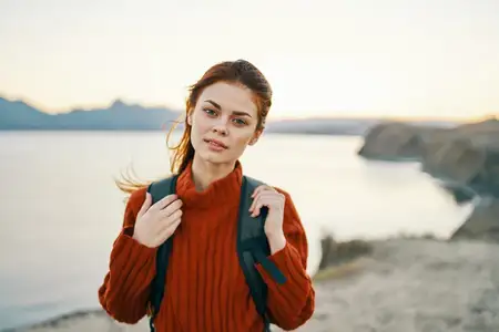 Женщина отдыхает на свежем воздухе в горах у моря, на пляже с песчаным берегом, рядом рюкзак
