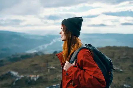 Женщина путешествует в горах, на пейзаже, с рюкзаком, в красной куртке и шляпе, модель