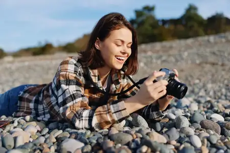Уличная сцена: улыбающаяся женщина-фотограф на галечном пляже с камерой в руках