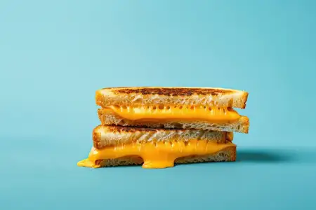 Аппетитный сэндвич с жареным сыром, идеально сложенный стопкой с вытекающим расплавленным сыром чеддер на ярком синем фоне