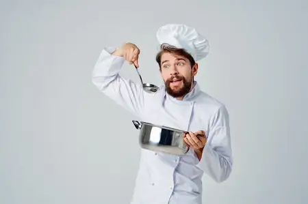 Шеф-повар с кастрюлей в руках на кухне ресторана занимается приготовлением еды