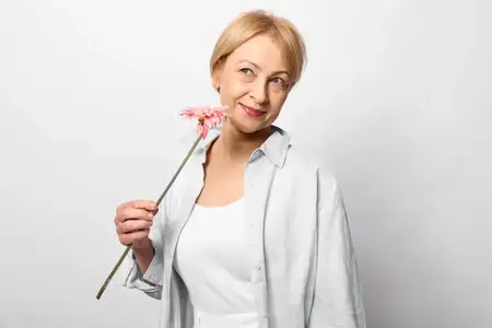 Пожилая женщина улыбается, держа розовый цветок в студийном портрете