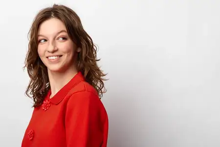 Улыбающаяся женщина в красном трикотаже смотрит в сторону на однотонном белом фоне
