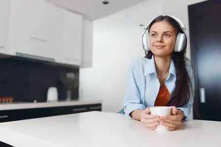 Молодая женщина слушает музыку в наушниках, наслаждаясь чашкой кофе за столом