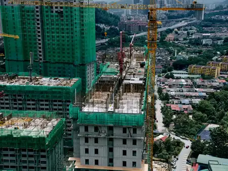 Вид с высоты птичьего полёта на строительную площадку, где возводятся высотные здания, окружённые зеленью и городской застройкой
