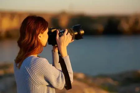 Женщина с профессиональным фотоаппаратом на открытом воздухе в горах фотографирует закат у моря