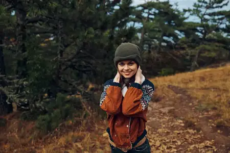 Счастливая молодая женщина улыбается на живописной осенней туристической тропе, проходящей через лес, окружённый разноцветной листвой
