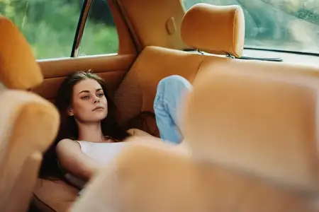 Расслабленная молодая женщина в винтажном автомобиле, одетая в повседневную одежду, в окружении природы