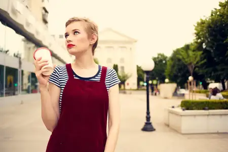 Симпатичная женщина со стаканом напитка прогуливается на свежем воздухе, ведя активный образ жизни