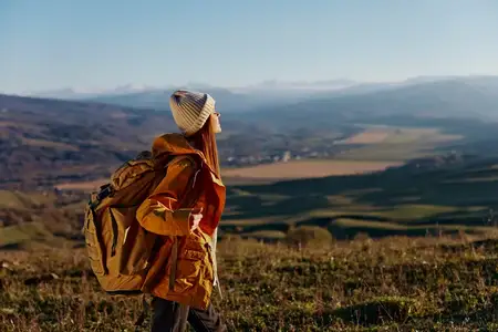 Женщина в жёлтой куртке и шапке с рюкзаком путешествует по горам