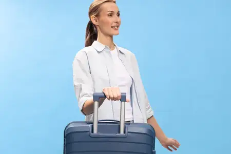 Улыбающаяся женщина держится за ручку чемодана на голубом фоне