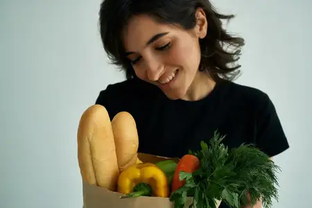 Весёлая женщина в чёрной футболке, пакет с продуктами, овощи, здоровая еда, крупный план