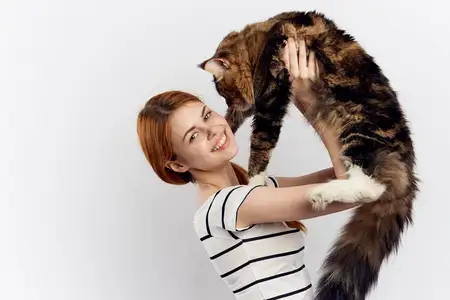 Рыжеволосая женщина держит в руке кота, полосатая футболка, светлый фон, домашний питомец