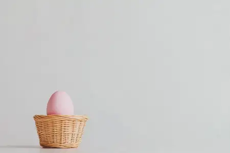 Нежное розовое пасхальное яйцо в плетеной корзине на мягком светлом фоне, олицетворяющее темы весны, обновления и праздничной радости во время пасхальных торжеств