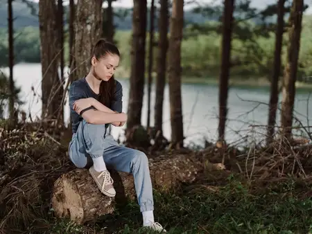 Задумчивая женщина сидит на природе, размышляя у кромки воды