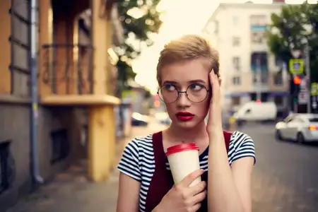 Женщина с короткой стрижкой в очках на прогулке на открытом воздухе, отдых с чашкой напитка