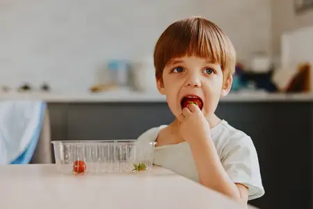Маленький мальчик с игривым выражением лица наслаждается свежим виноградом, сидя за стильным кухонным столом
