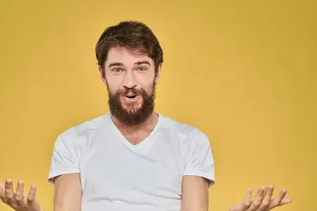 Крупный план эмоционального бородатого мужчины в белой футболке на ярко-жёлтом фоне