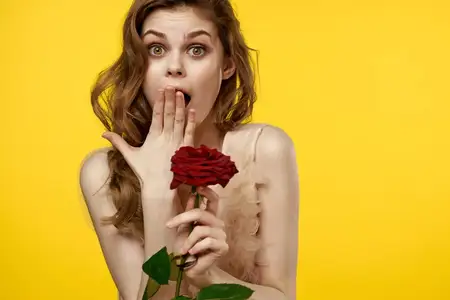 Романтичная женщина в вечернем платье с красной розой на жёлтом фоне, обрезанный вид, портрет