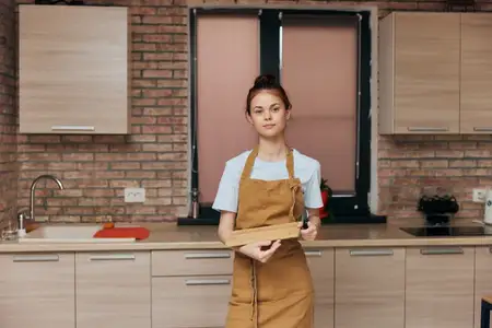 Домохозяйка в фартуке на кухне с разделочной доской и ножом