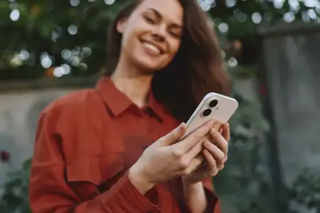 Жизнерадостная женщина на открытом воздухе держит смартфон, одетая в повседневную рубашку ржавого цвета
