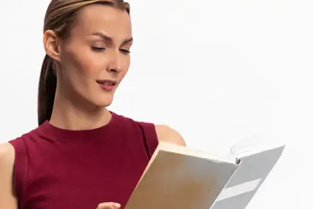 Сосредоточенная молодая женщина читает книгу в красном топе на белом фоне