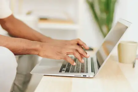 Улыбающийся афроамериканский мужчина работает за ноутбуком в современном домашнем офисе