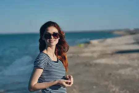Путешественница в солнцезащитных очках и футболке отдыхает на пляже у моря в горах